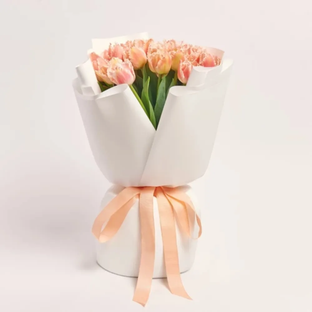 Peach carnation bouquet wrapped in white paper with a soft peach ribbon