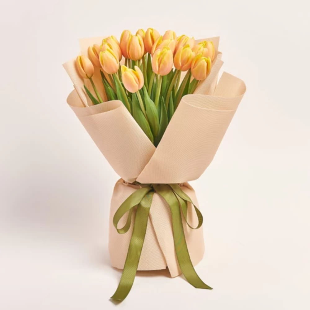 A bouquet of peach tulips wrapped in cream kraft paper and tied with an olive green satin ribbon