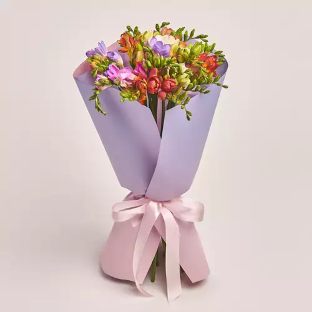 A colorful mixed freesia bouquet wrapped in lavender paper and tied with a pink satin ribbon