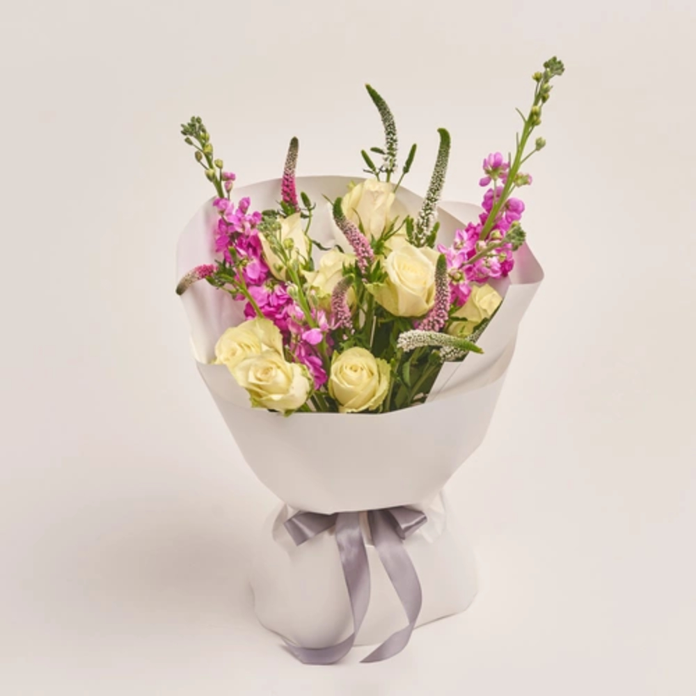 Elegant mixed flower bouquet with white roses and pink blooms wrapped in white paper with a silver ribbon