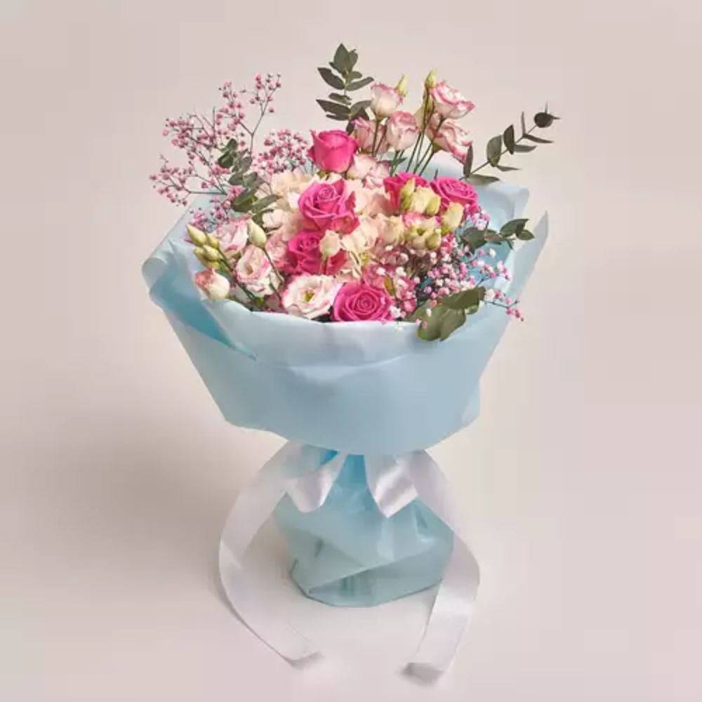 Mixed flower bouquet with pink roses and fillers wrapped in light blue paper with a white ribbon