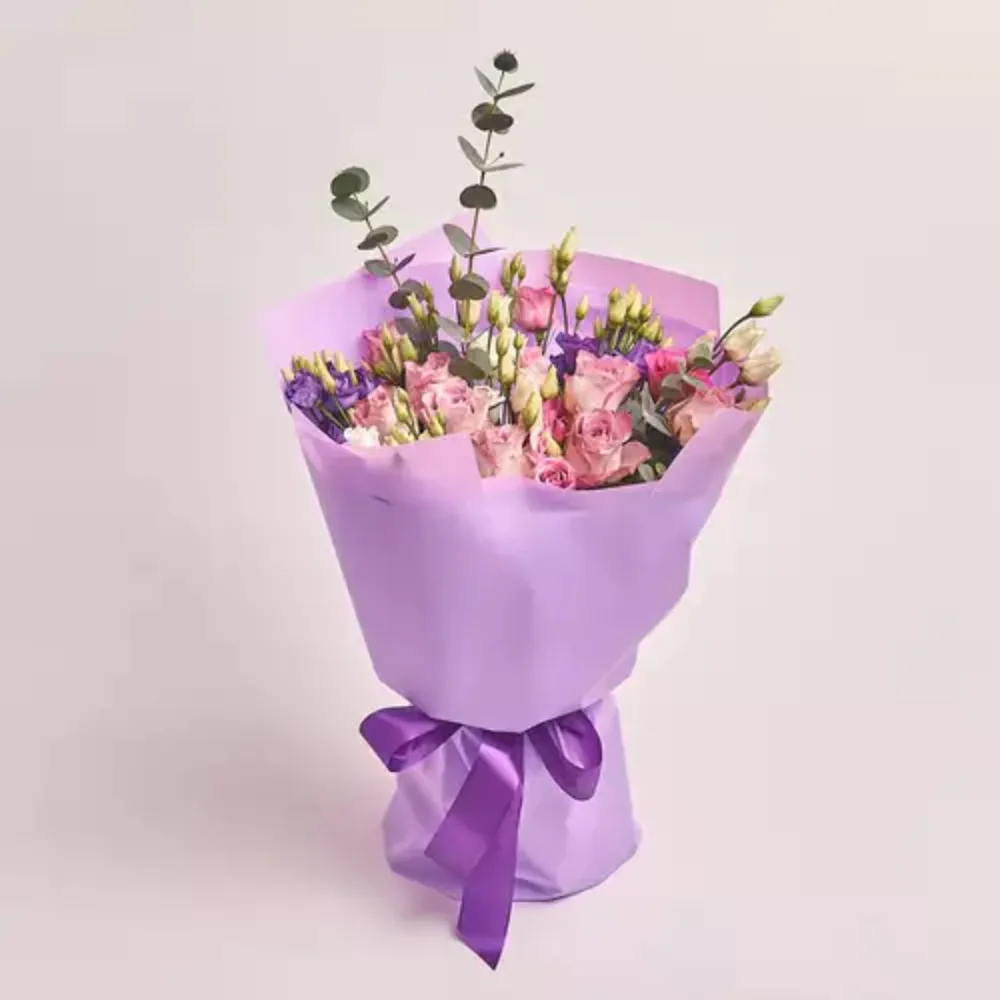 Mixed pastel flower bouquet with roses and greenery wrapped in lavender paper and tied with a purple ribbon