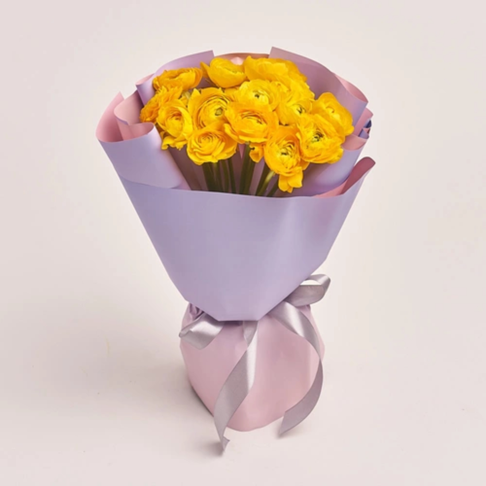 Yellow ranunculus flower bouquet wrapped in pastel pink and lavender paper with a ribbon bow.