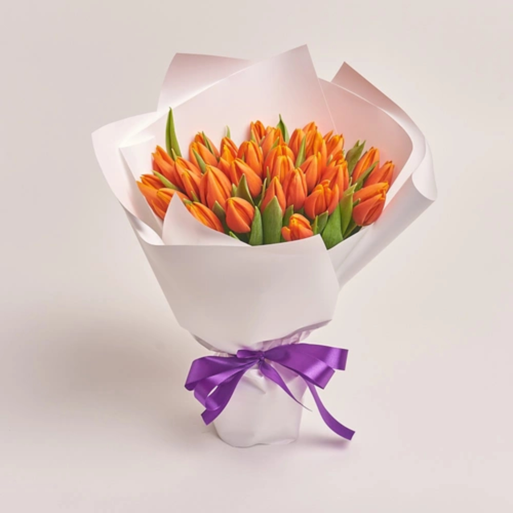 A bouquet of bright orange tulips wrapped in white paper and tied with a purple satin ribbon