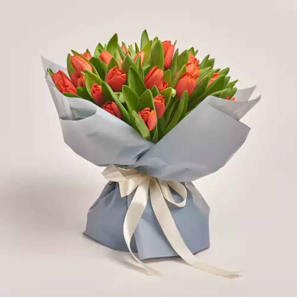 Fresh orange tulip bouquet with green foliage wrapped in soft blue paper and tied with a cream ribbon, elegant floral gift by Favish Blooms Dubai