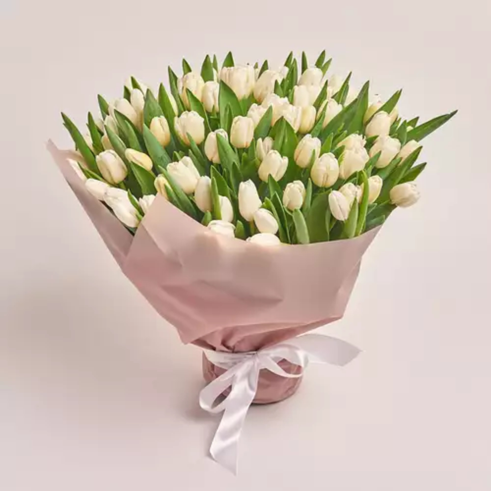 A large bouquet of cream white tulips wrapped in blush pink paper and tied with a white ribbon