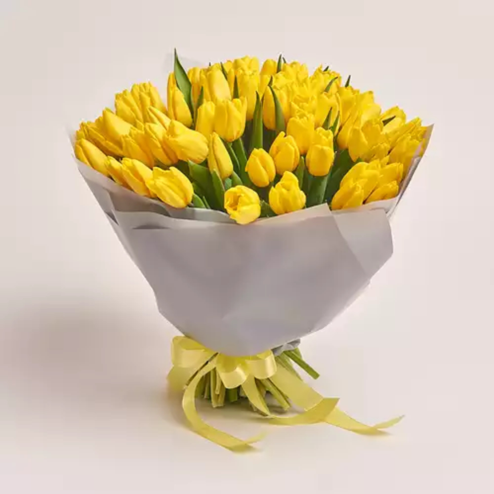 A large bouquet of bright yellow tulips wrapped in grey paper and tied with a yellow ribbon