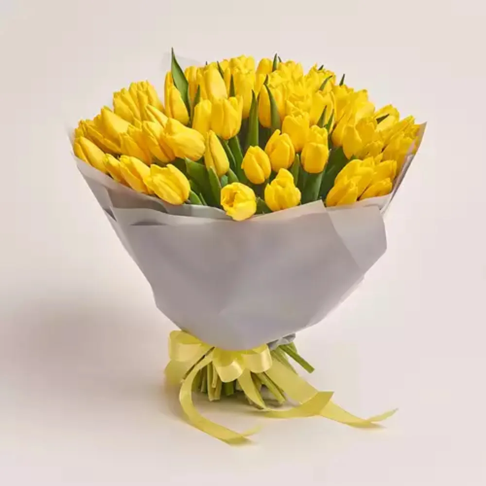 A large bouquet of bright yellow tulips wrapped in grey paper and tied with a yellow ribbon