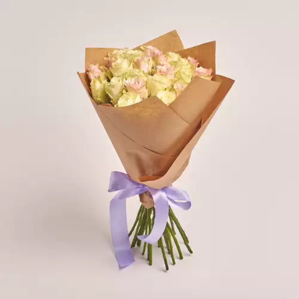A bouquet of cream and pink roses wrapped in kraft paper and tied with a lavender satin ribbon
