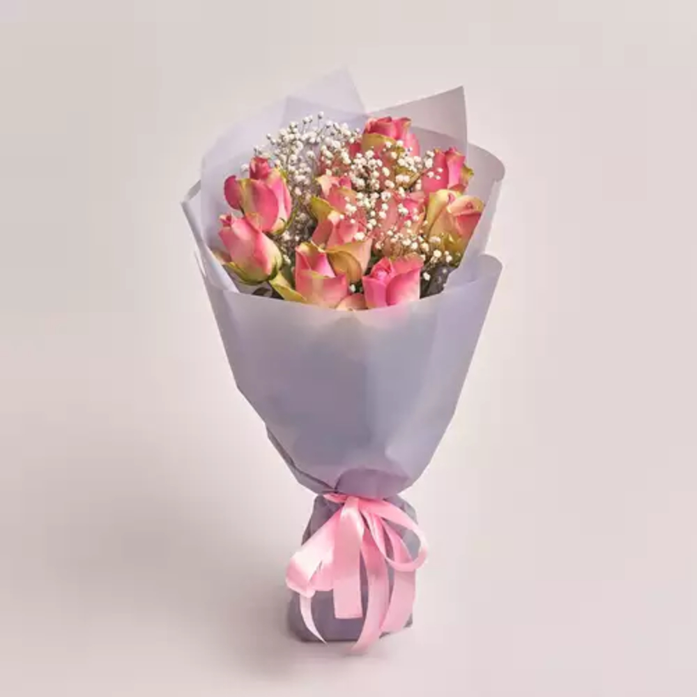 A bouquet of pink roses and white baby's breath wrapped in grey paper and tied with a pink satin ribbon