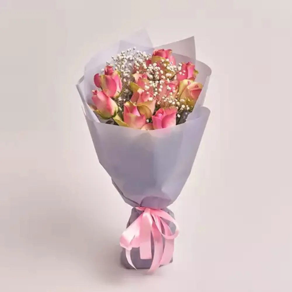 A bouquet of pink roses and white baby's breath wrapped in grey paper and tied with a pink satin ribbon