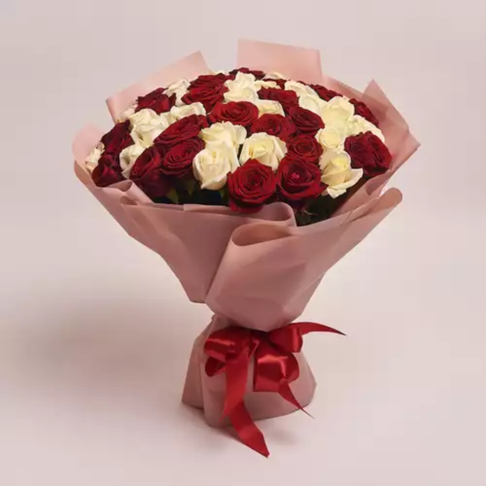 A large bouquet of mixed red and white roses wrapped in blush pink paper and tied with a red satin ribbon