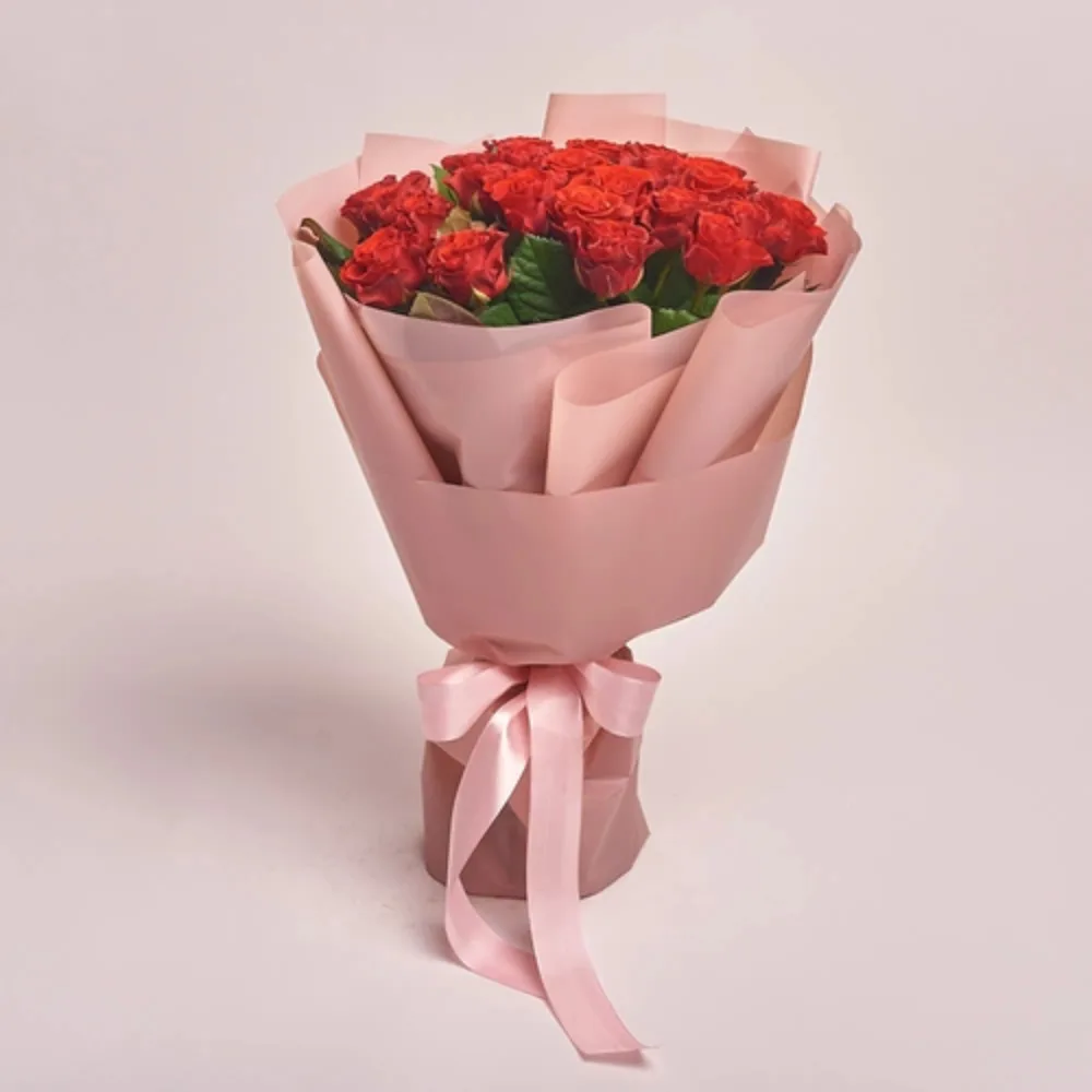 A bouquet of red roses wrapped in blush pink paper and tied with a pink satin ribbon