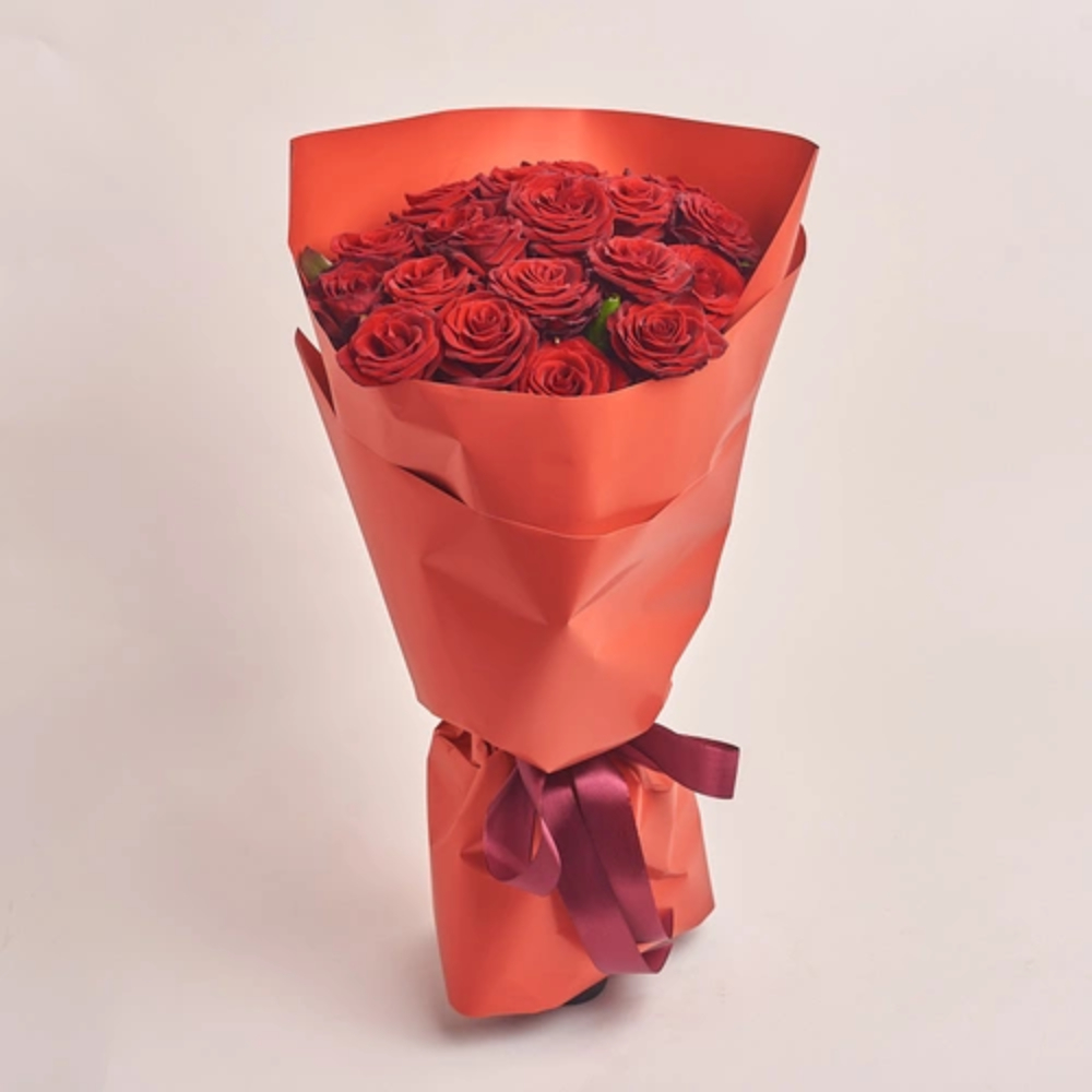 A bouquet of red roses wrapped in red paper and tied with a burgundy satin ribbon