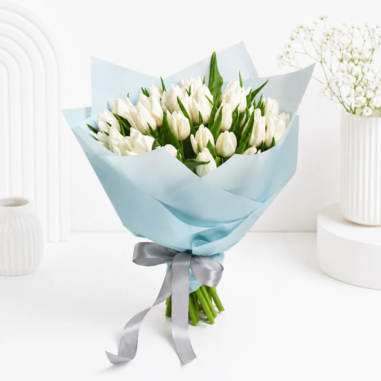Elegant white tulip bouquet wrapped in pastel blue paper and finished with a silver ribbon, a graceful sympathy floral arrangement perfect for expressing condolences, support, and remembrance.