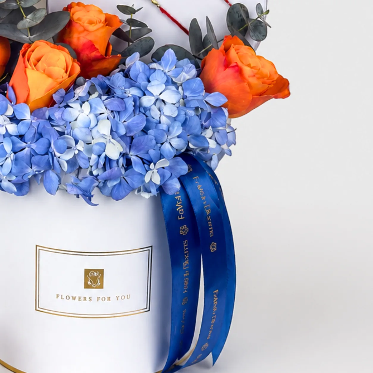 Close-up of a 'Flowers For You' box with orange roses, blue hydrangeas, and blue ribbon detail