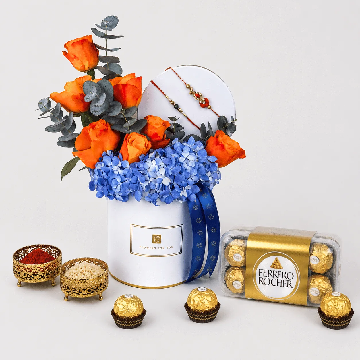 Rakhi gift hamper with orange roses, blue hydrangeas, and Ferrero Rocher chocolates.