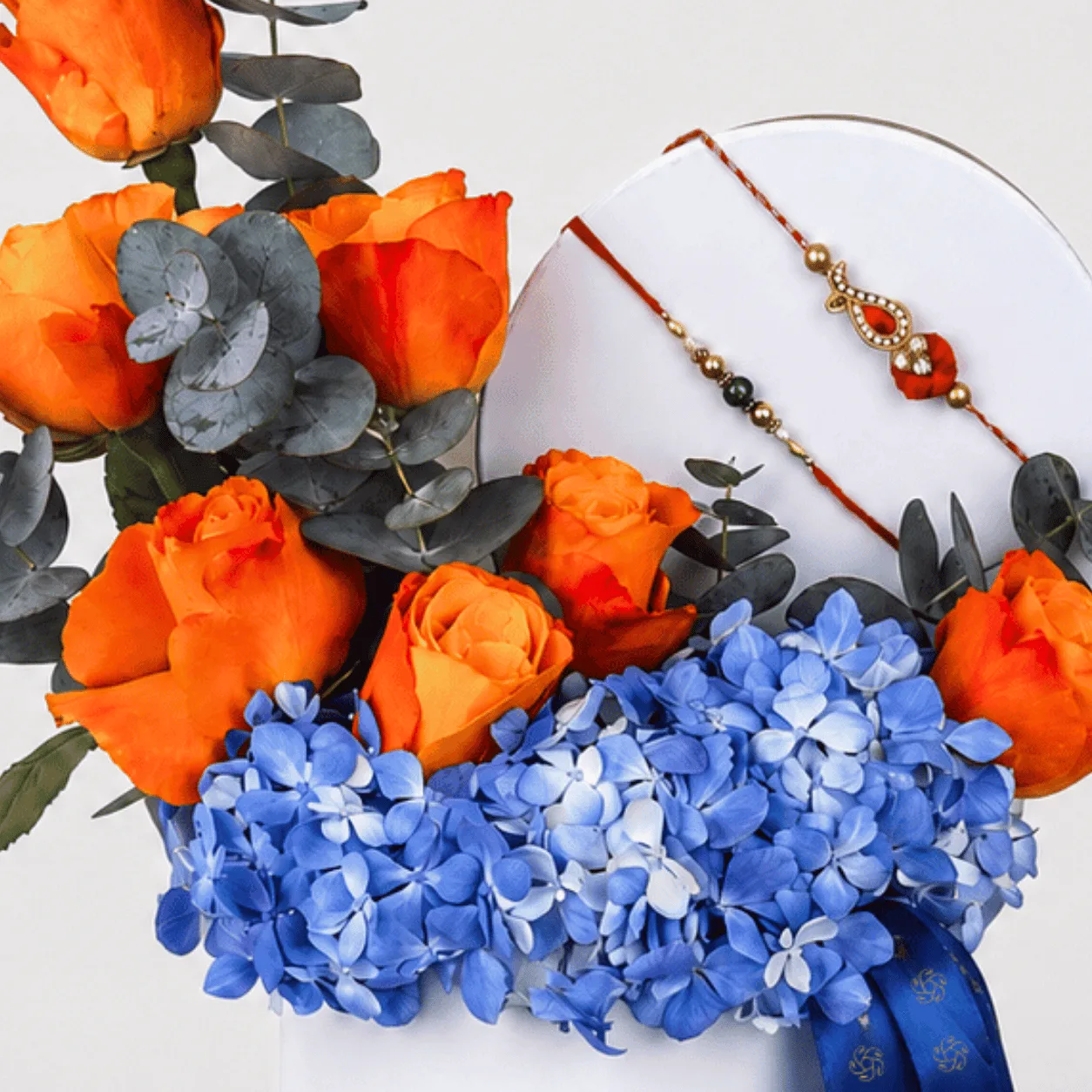 Close-up of orange roses and blue hydrangeas with two decorative Rakhi threads.