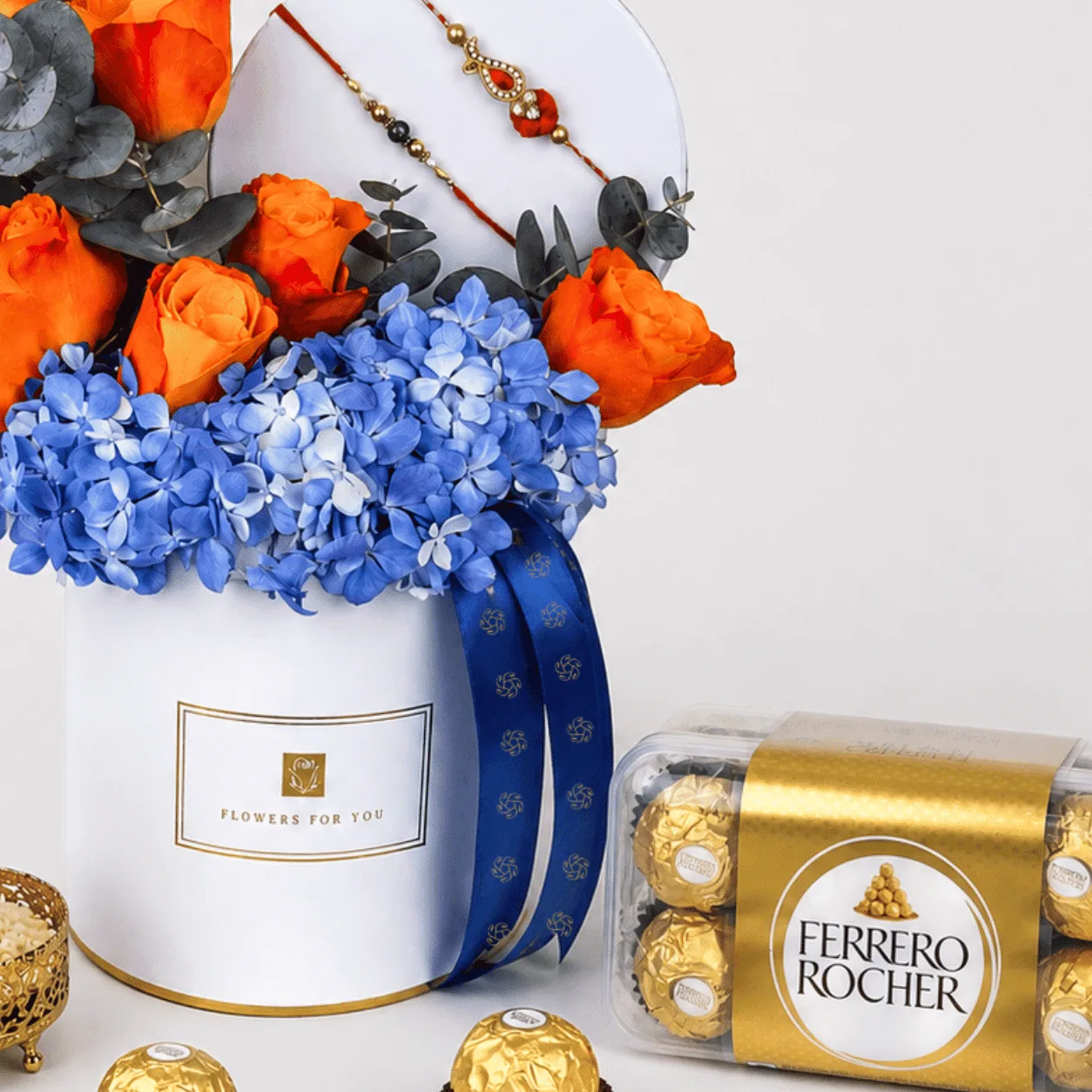 Rakhi flower box with orange roses, blue hydrangeas, and Ferrero Rocher chocolates.