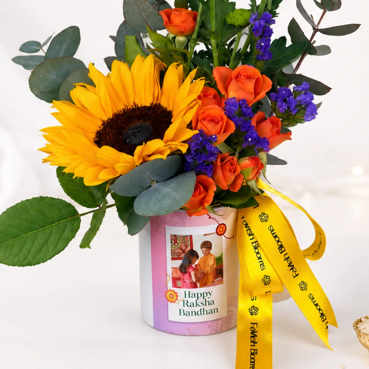 Raksha Bandhan flower arrangement featuring sunflower, roses and seasonal blooms in a ceramic mug