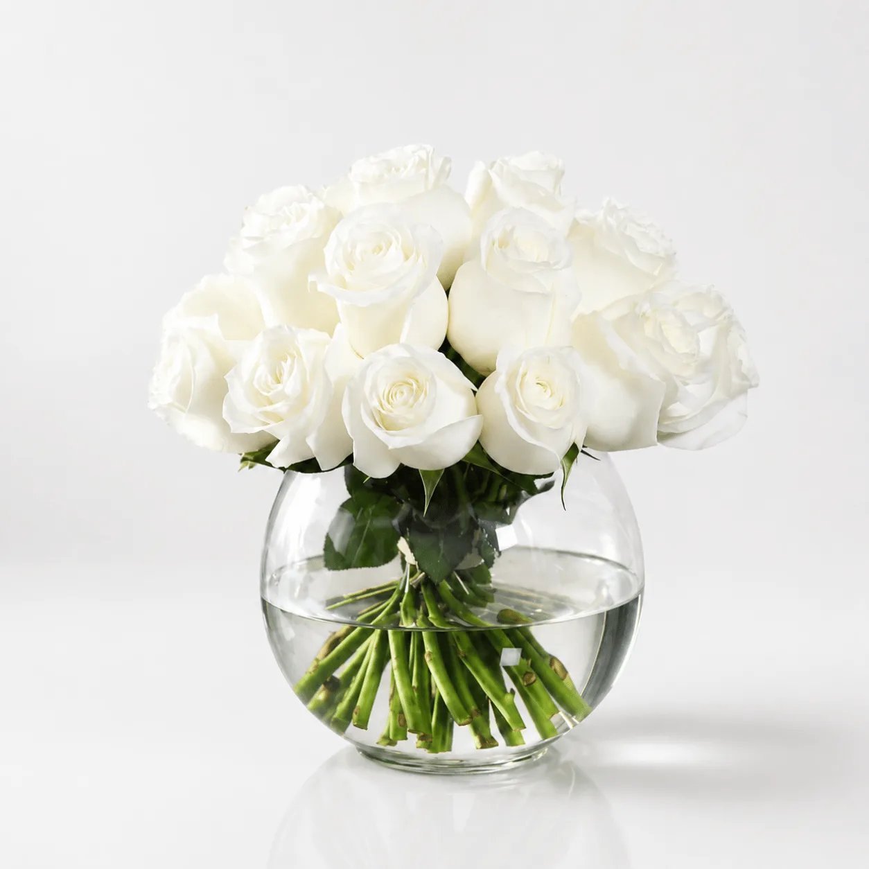 Luxury white rose vase arrangement in a transparent fish bowl with fresh greenery