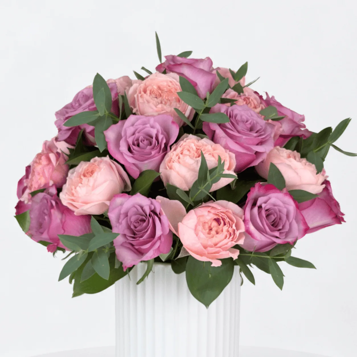 Deep purple roses and pink Juliette spray roses in a ceramic pot for anniversary celebrations.