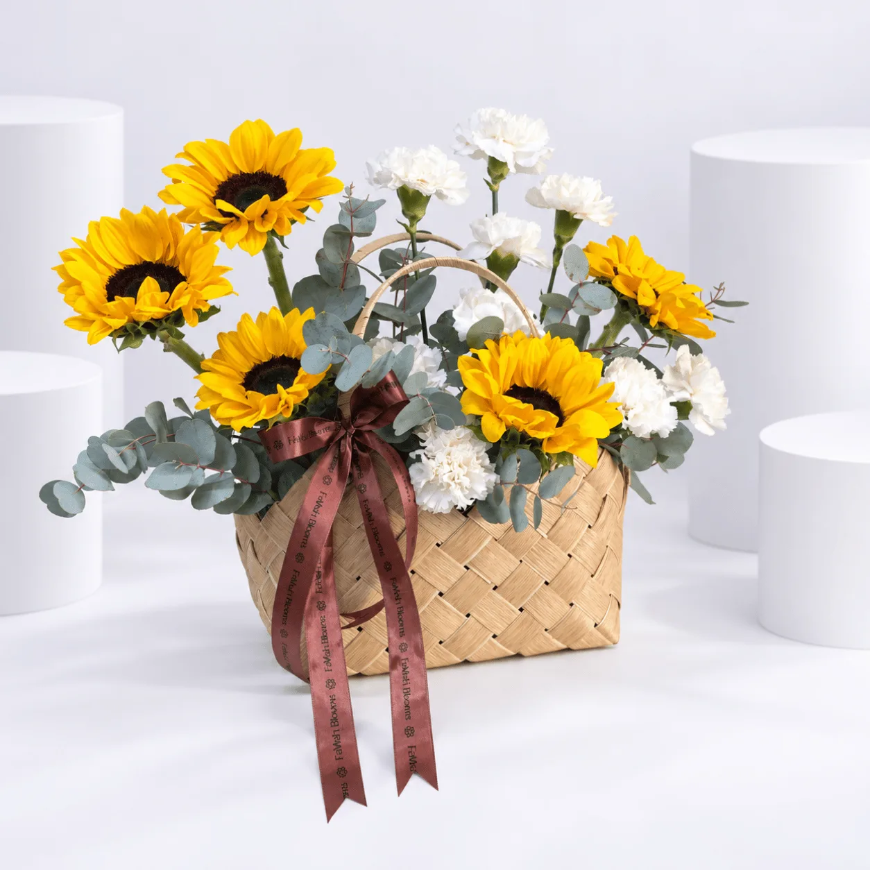 Fresh yellow sunflower and white carnation arrangement in a rustic wicker basket for birthday and anniversary gifting.