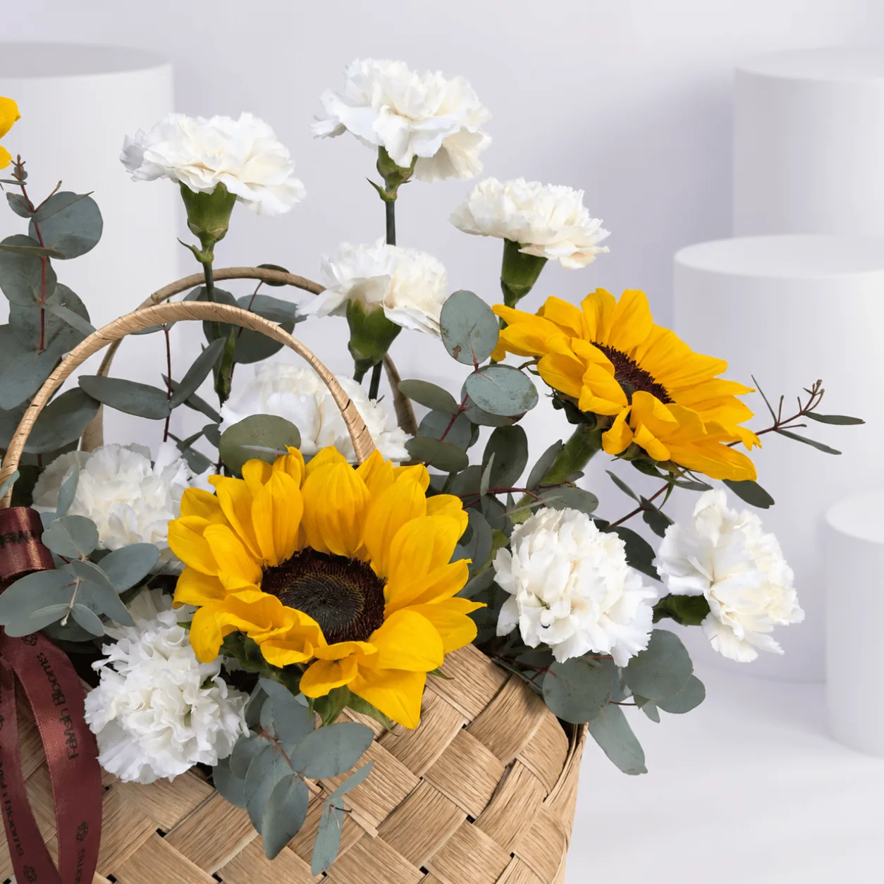 Beautiful Golden Hour Flower Basket with 5 yellow sunflowers, 9 white carnations and fresh eucalyptus foliage.