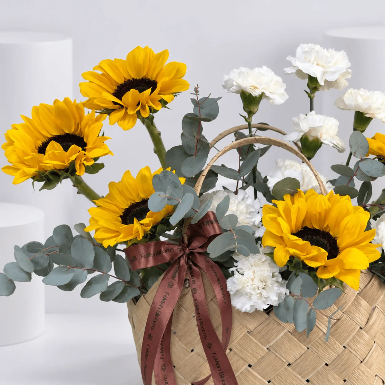 The Golden Hour Flower Basket featuring fresh yellow sunflowers, white carnations and eucalyptus in a woven wicker basket.
