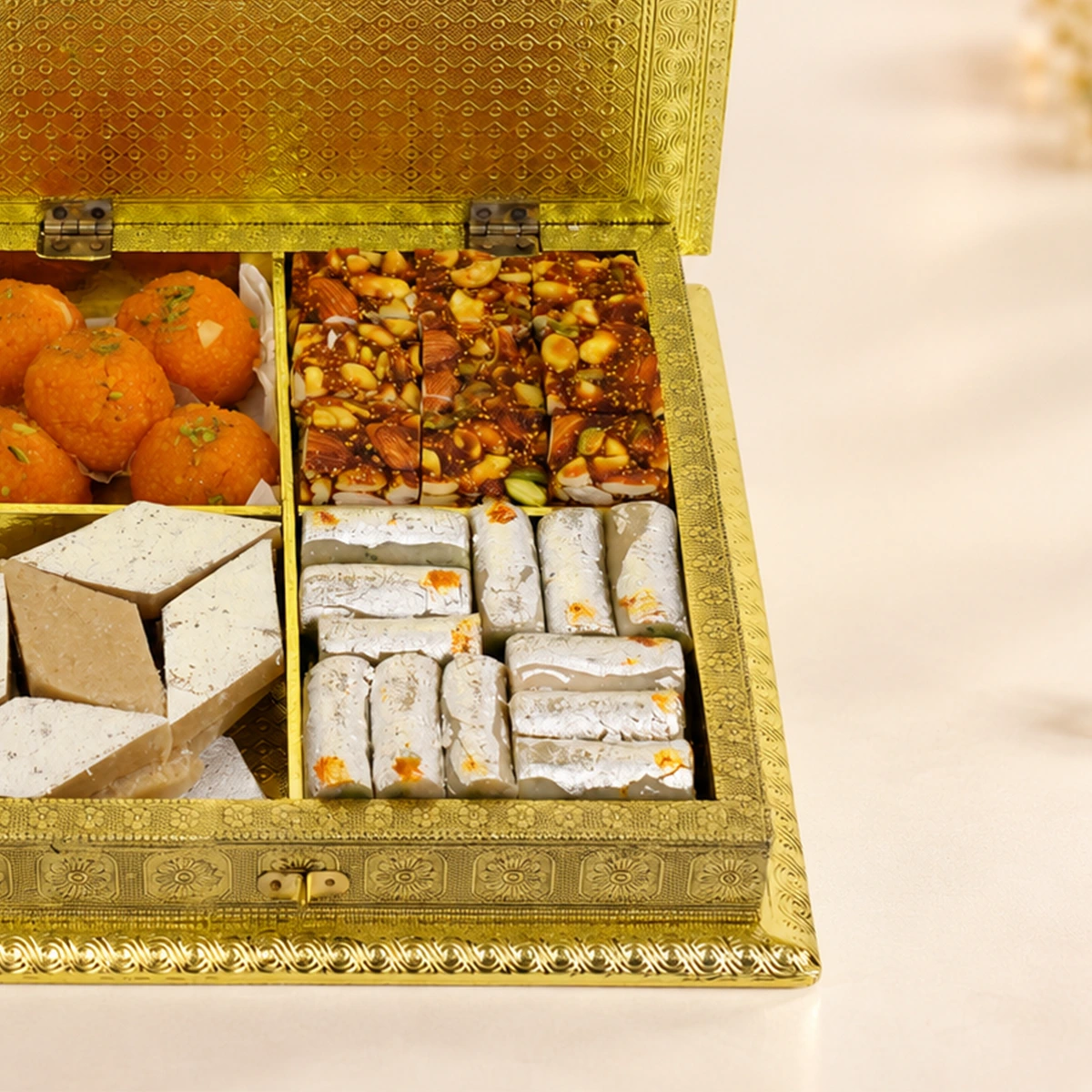 Close-up of dry fruit chikki and silver-coated Indian sweets in a luxury Diwali gift box.