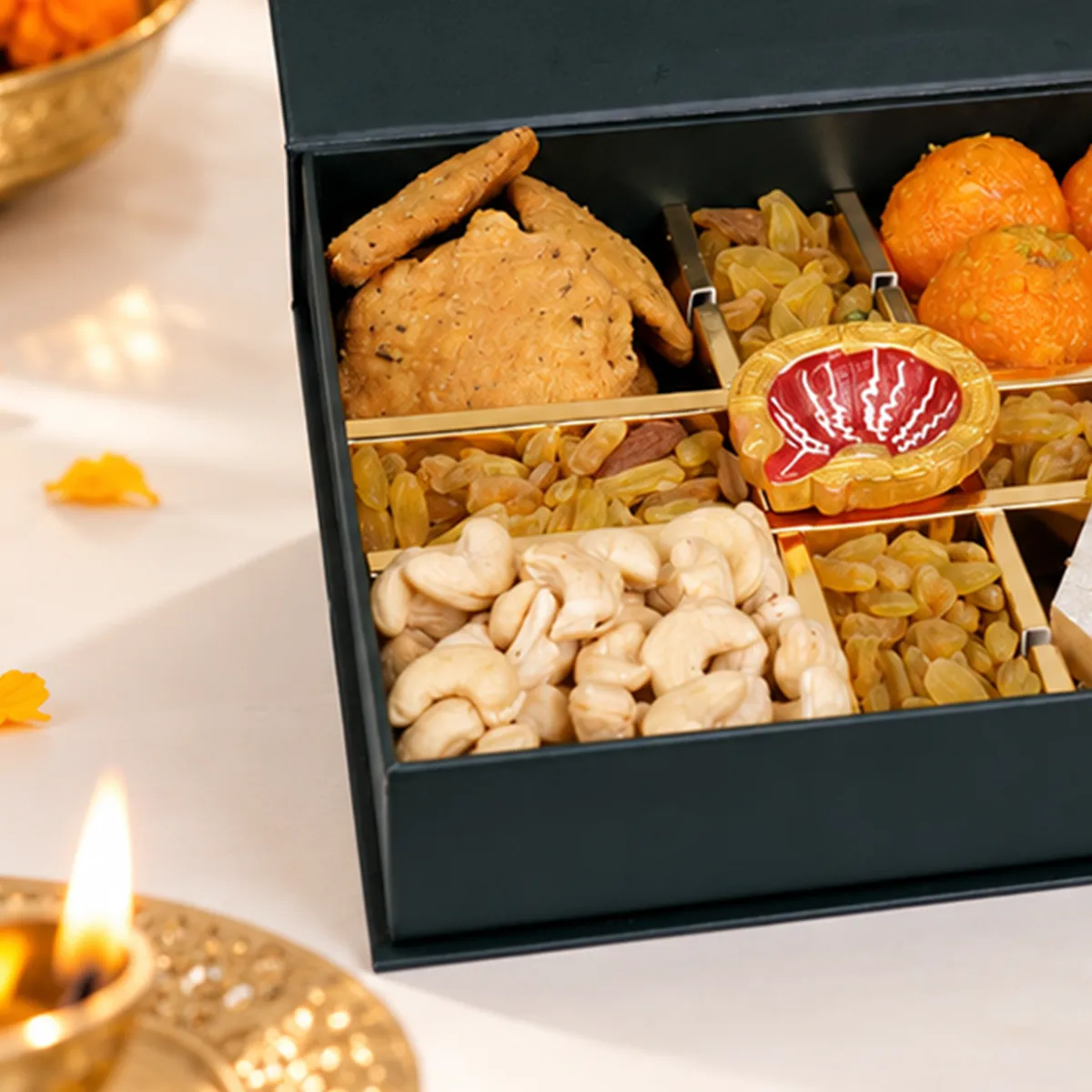 Close-up of luxury Diwali hamper featuring crispy mathri, premium cashews, golden raisins, and decorative diya.