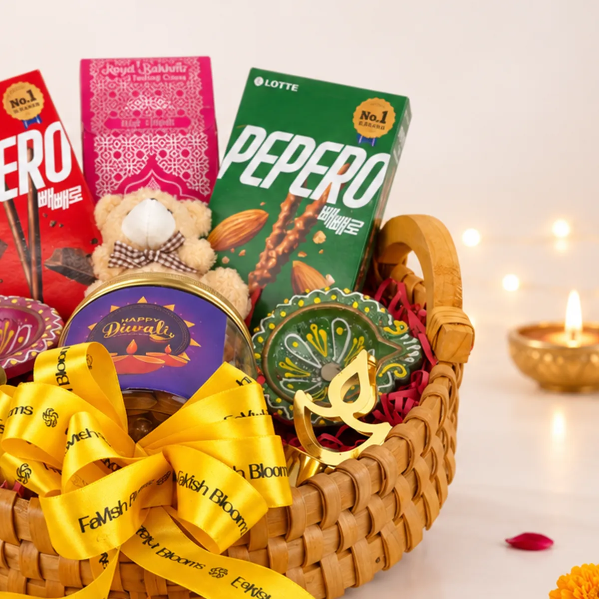 Close-up of Diwali gift hamper featuring almond Pepero, teddy bear, chocolates, and decorative diya.