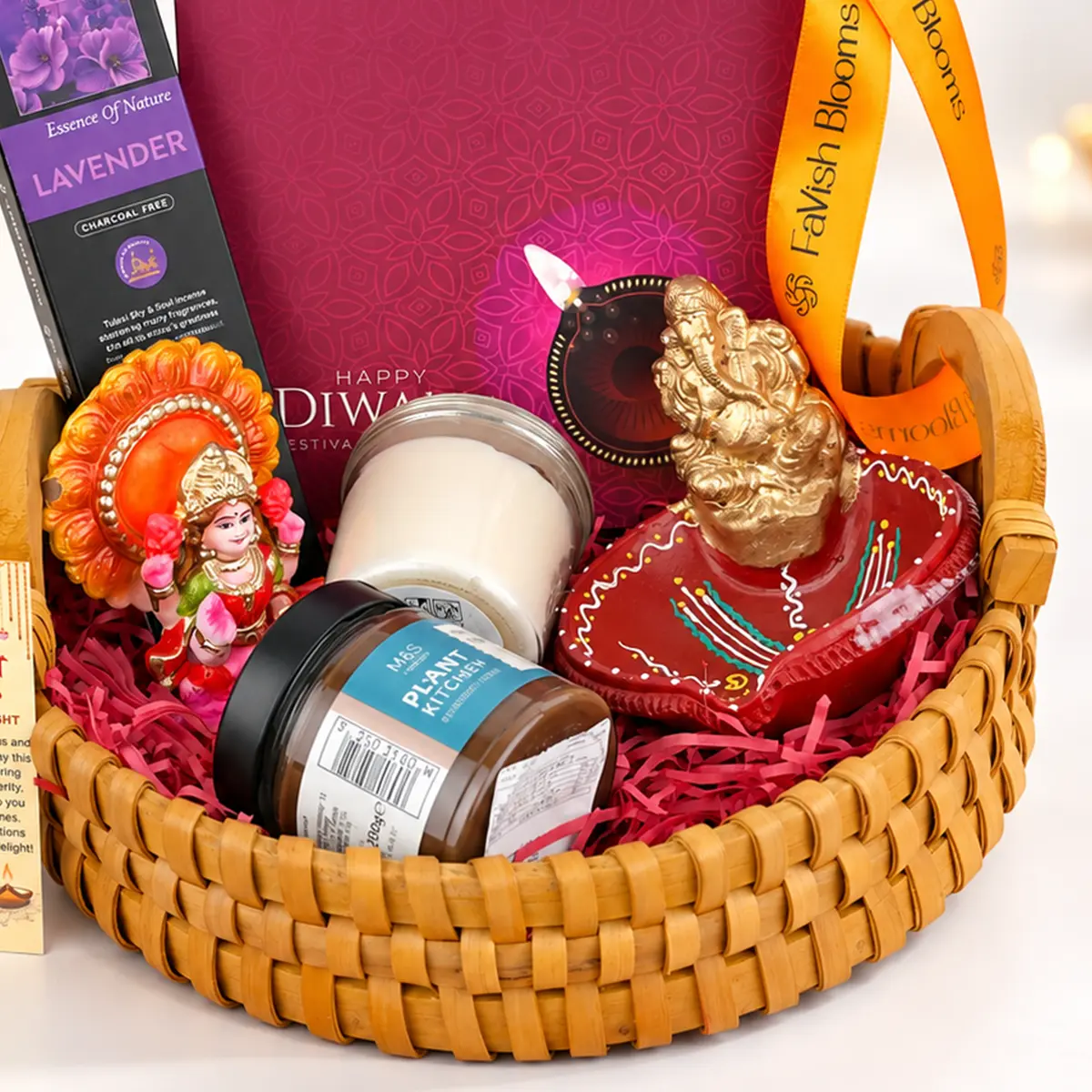 Close-up of luxury Diwali gift hamper featuring golden Ganesha idol, decorative diya, scented candles, lavender incense sticks, and wicker gift basket.