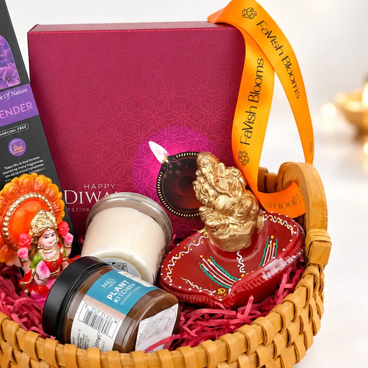 Detailed view of Diwali gift basket featuring a golden Lord Ganesha idol, handcrafted red diya, magenta festive gift box, and FaVish Blooms ribbon.
