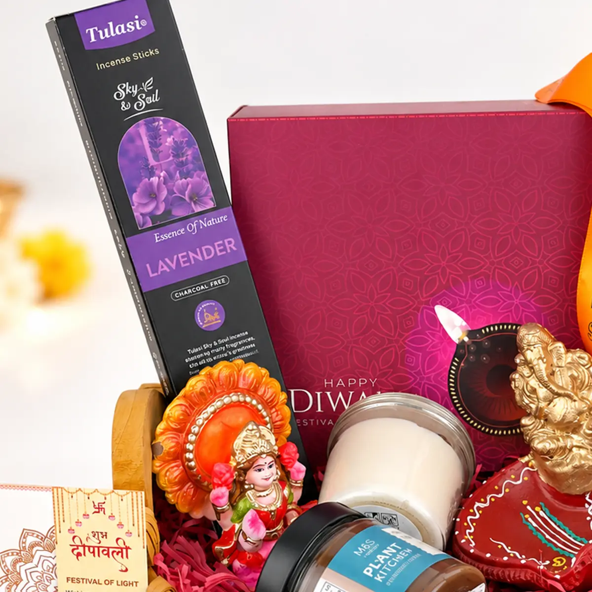 Close-up of Tulasi lavender incense sticks, Goddess Lakshmi idol, scented candle, and festive Diwali gift packaging.