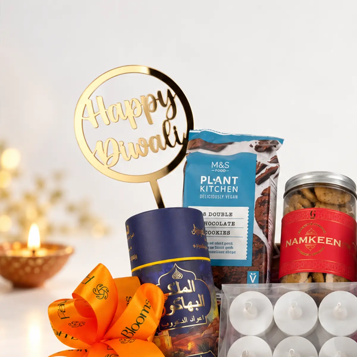 Close-up of golden Happy Diwali topper, FaVish Blooms orange satin ribbon, chocolate cookies, and festive incense packaging in a Diwali gift hamper.