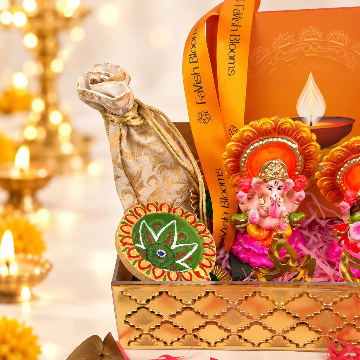Close-up of Diwali gift hamper with colorful Lord Ganesha idol, decorative rangoli diya, golden gift tray, and FaVish Blooms ribbon.