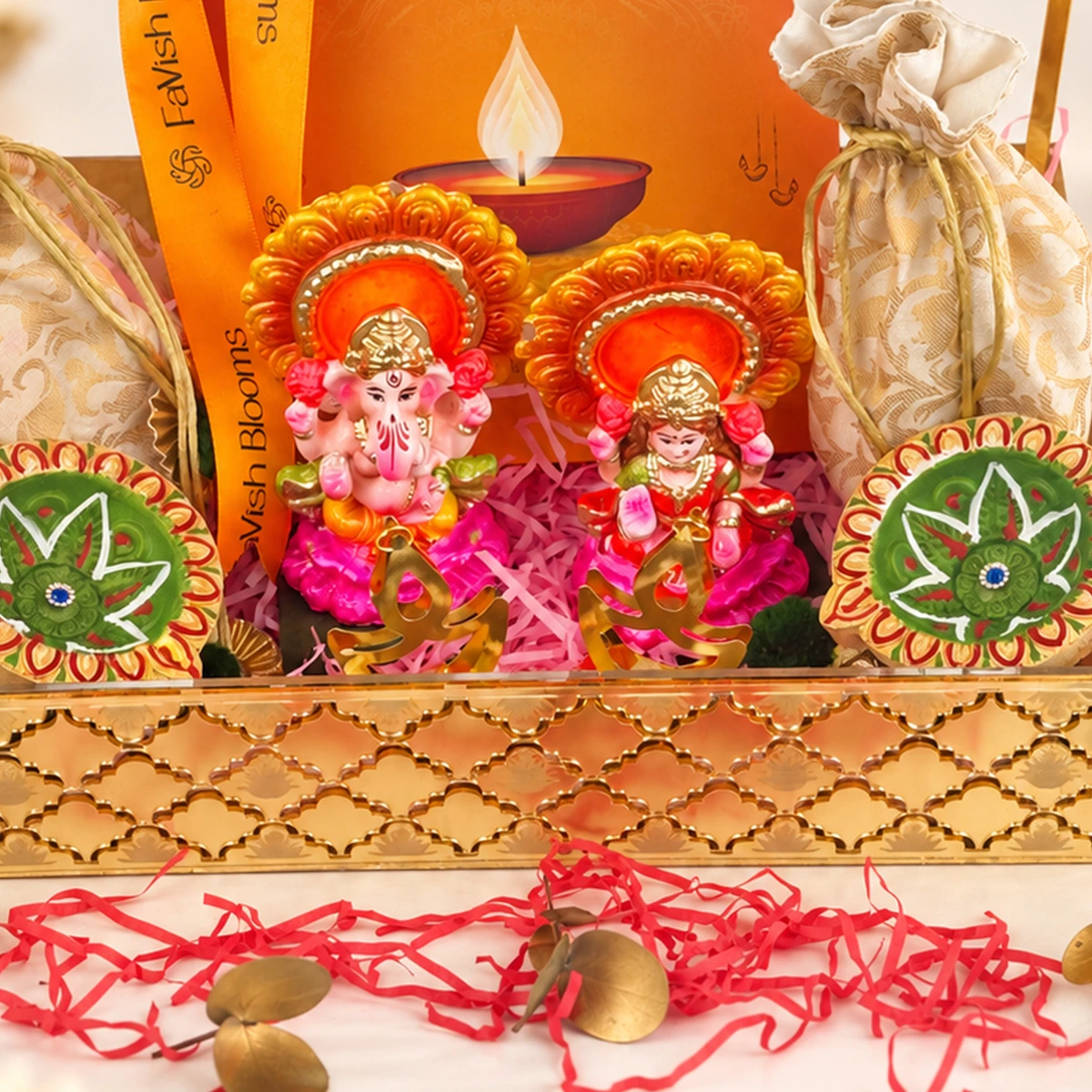 Diwali gift tray featuring Lord Ganesha and Goddess Lakshmi idols, colorful decorative diyas, festive gift pouches, and elegant gold packaging.