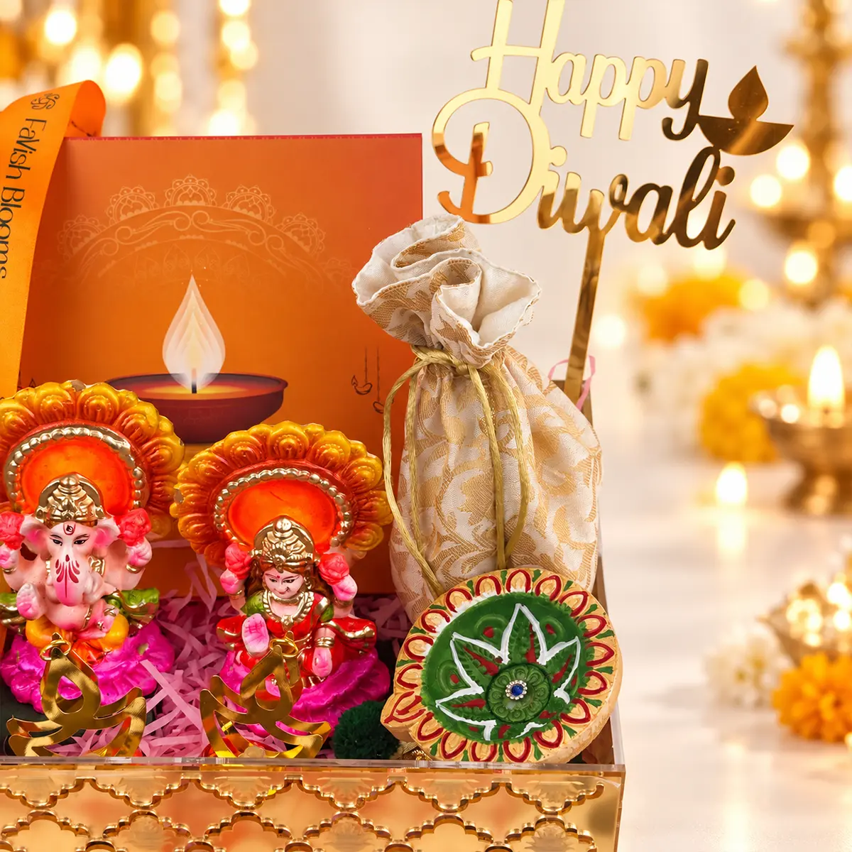 Close-up of gold Happy Diwali topper, festive gift pouch, decorative diya, and orange FaVish Blooms gift box with ribbon.