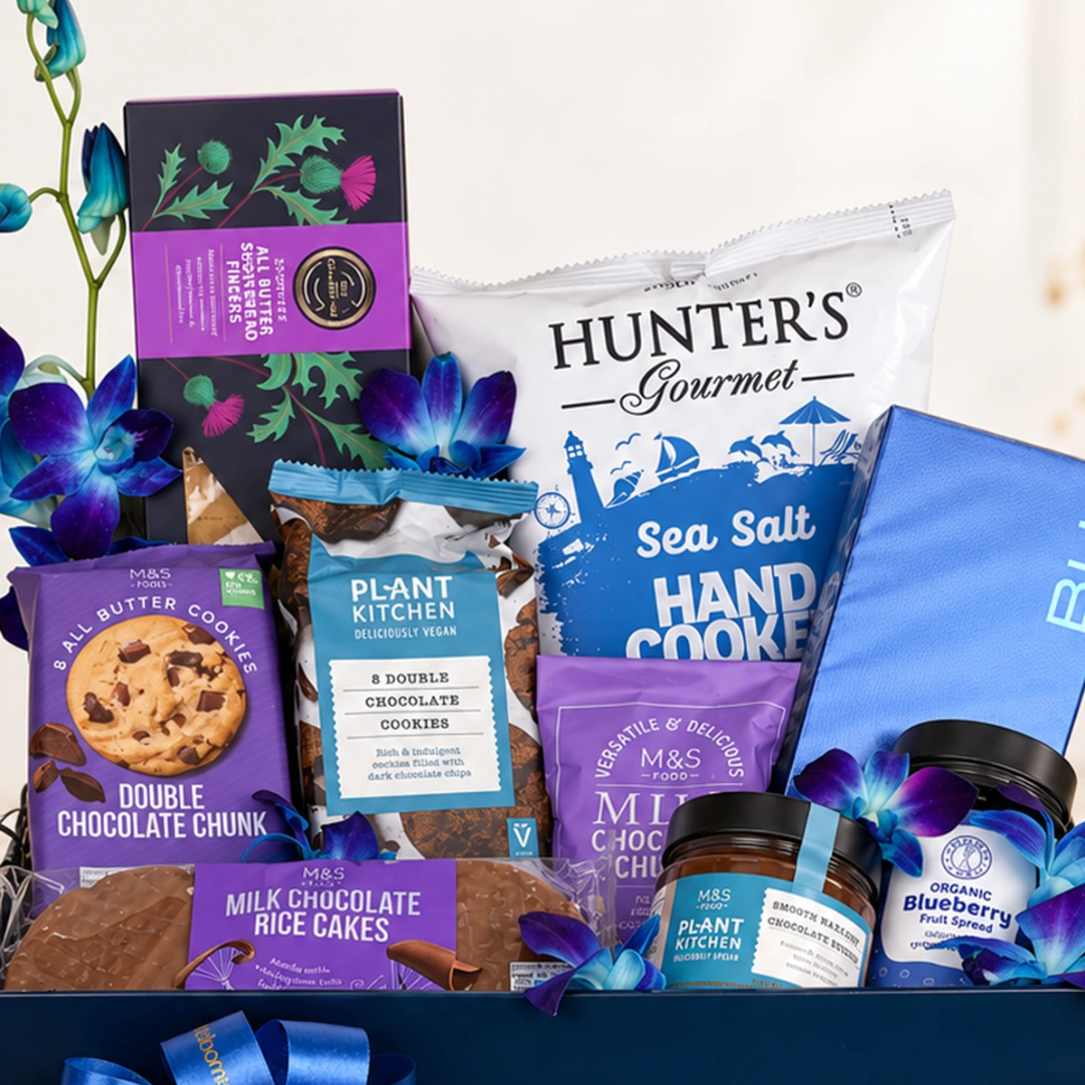Close-up of premium gift hamper with M&S chocolate cookies, Hunter's sea salt cookies, chocolate rice cakes, and gourmet spreads.