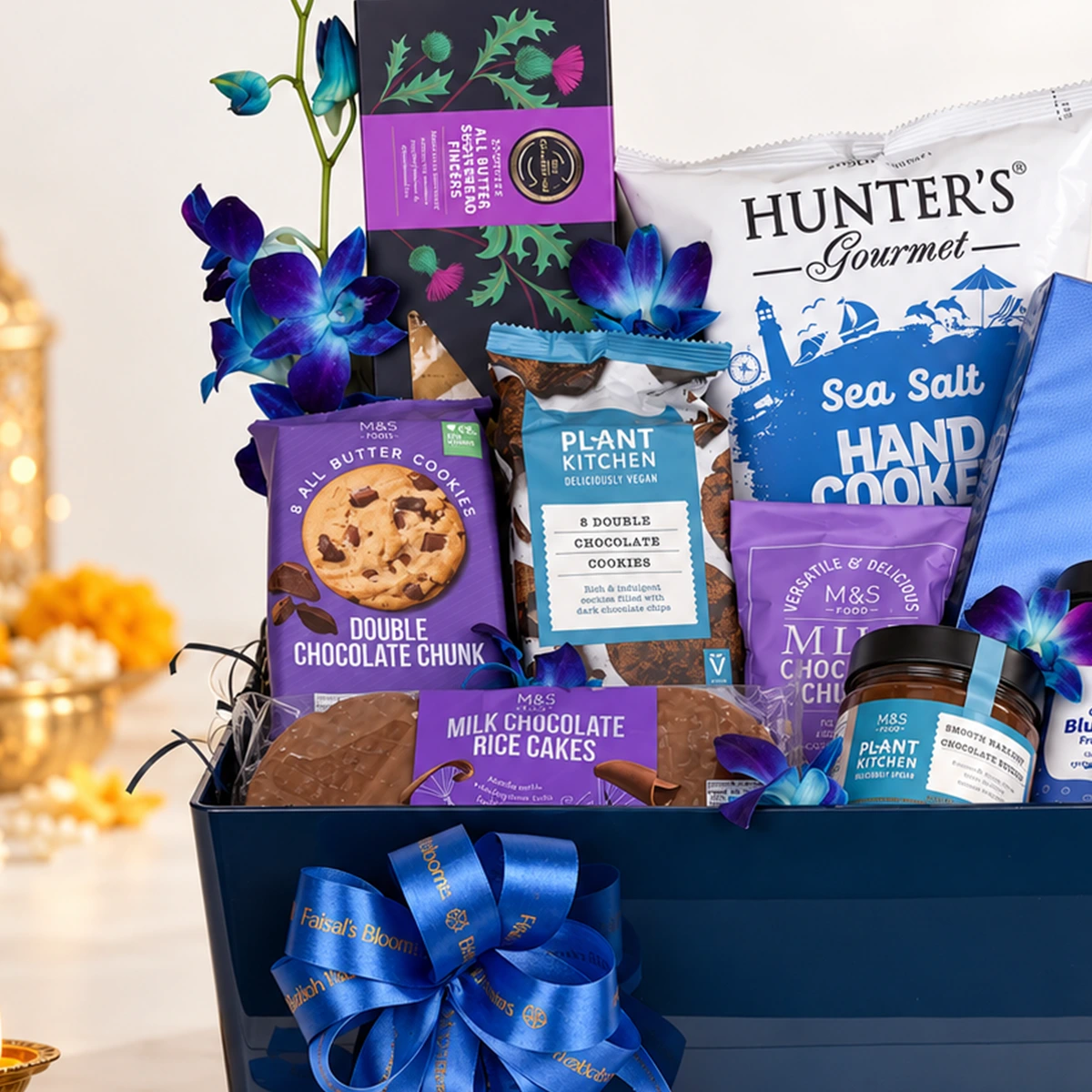 Elegant navy blue gourmet gift hamper with assorted chocolates, cookies, blue orchids, and a satin ribbon by FaVish Blooms.