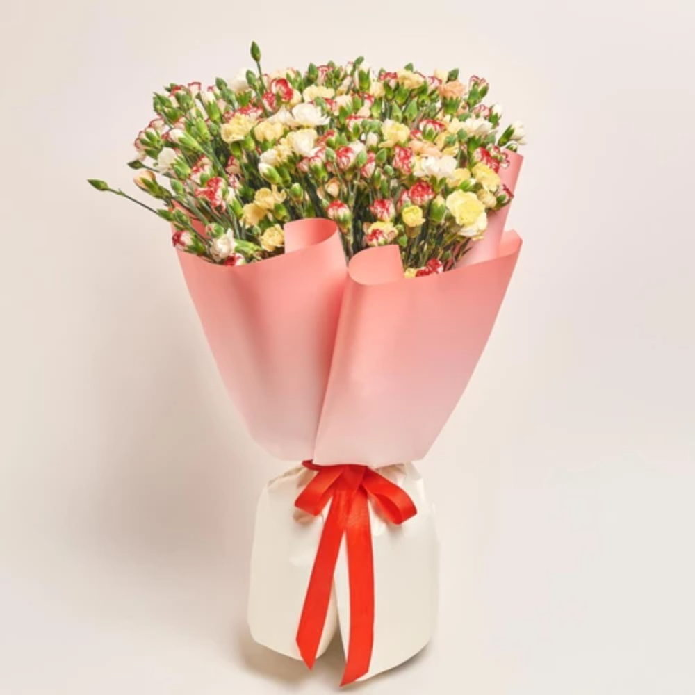 Mixed carnation bouquet in red, white, and yellow wrapped in pink paper with a red ribbon