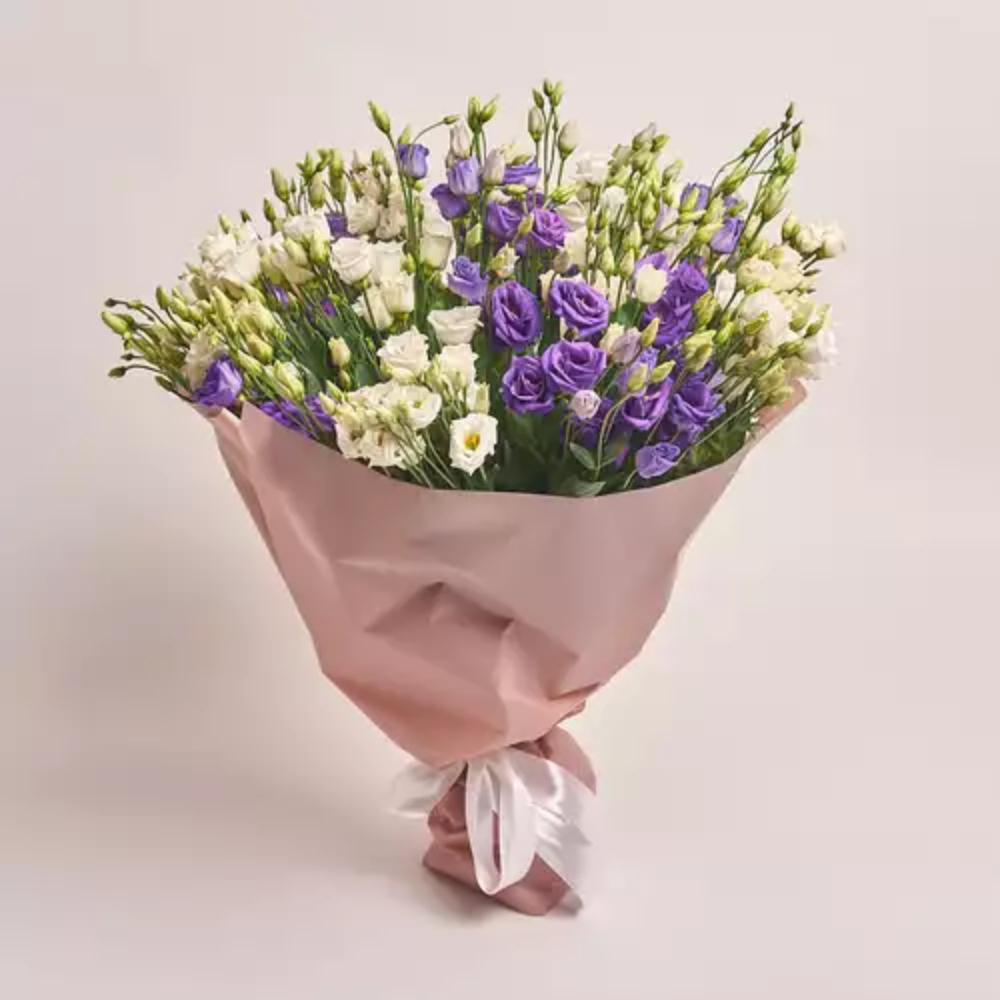 Mixed lisianthus bouquet in purple and white wrapped in blush pink paper with a white ribbon