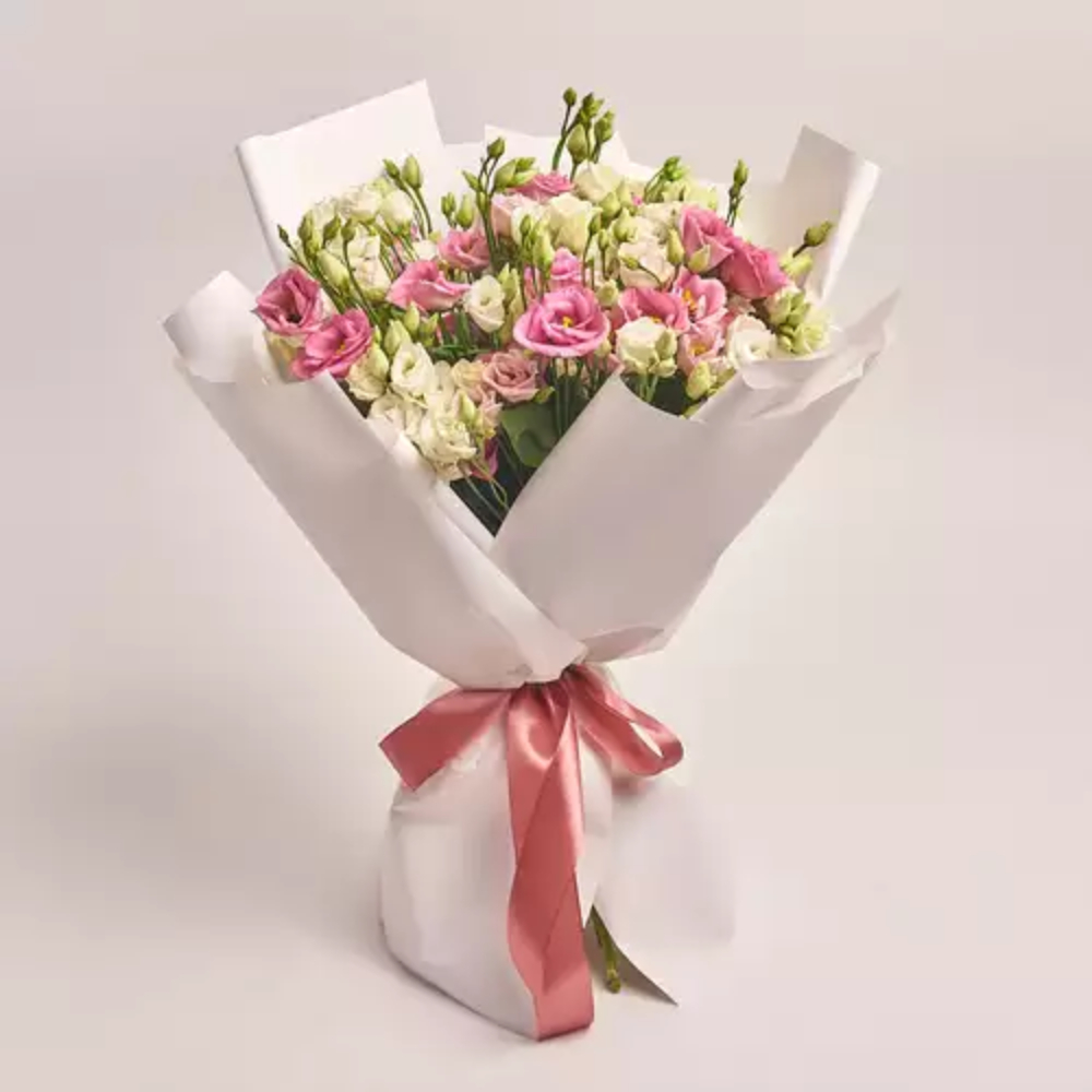 Mixed lisianthus bouquet in pink and white wrapped in white paper with a coral ribbon