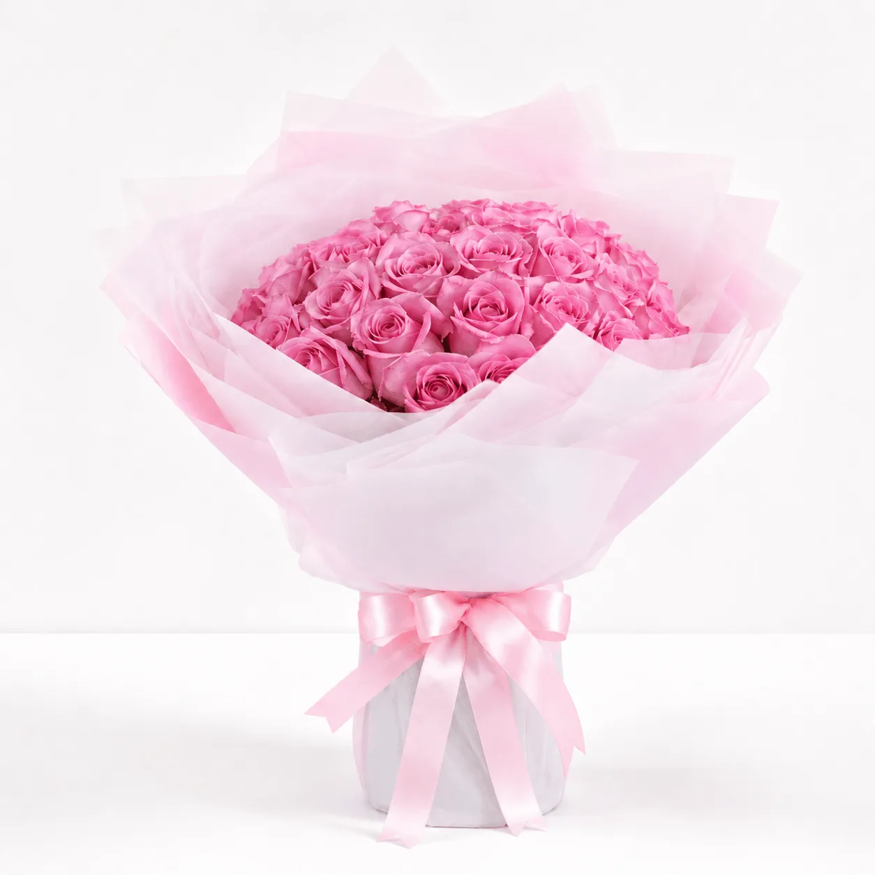 A bouquet of pink roses wrapped in soft pink tissue paper, tied with a pink satin ribbon, against a bokeh background.
