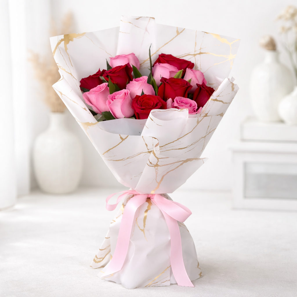 Red and pink roses wrapped in white and gold marble-print paper, tied with a pink ribbon.