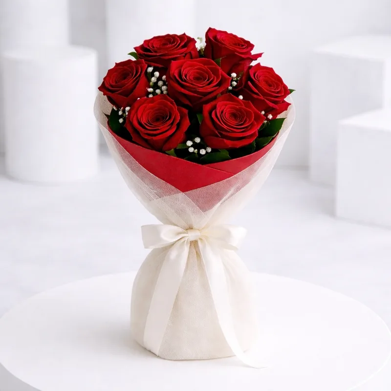 A bouquet of red roses with baby's breath wrapped in red and white tulle, tied with a cream ribbon.