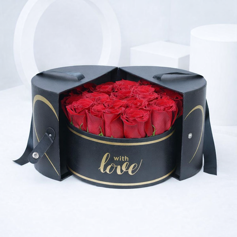 A black cylindrical gift box with gold "with love" script, opened to reveal a bouquet of red roses inside