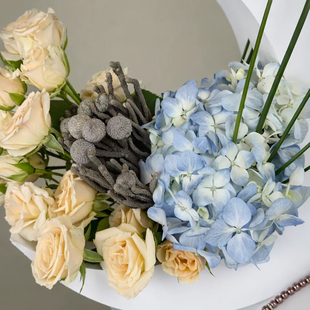Close-up of a floral arrangement featuring delicate light blue hydrangea petals, soft peach roses, and textured grey brunia berries.