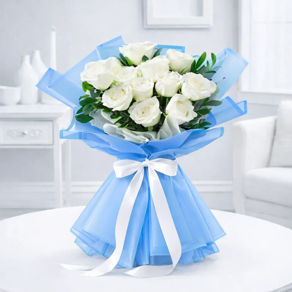 White roses bouquet wrapped in blue organza and tied with a white satin ribbon on a white table.